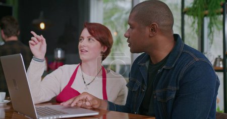 Téléchargez les photos : Deux employés masculins et féminins devant un ordinateur portable assis dans un restaurant de petite entreprise vérifiant les commandes en ligne ensemble - en image libre de droit