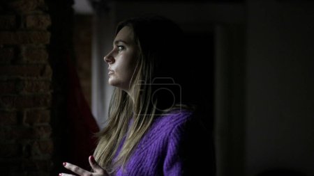 Téléchargez les photos : Jeune femme anxieuse debout près de la fenêtre préoccupée par des problèmes de vie - en image libre de droit