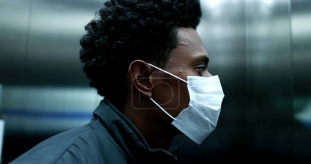 Téléchargez les photos : Black african man putting on covid mask inside elevator and stepping outside - en image libre de droit