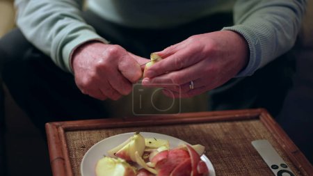 Téléchargez les photos : Gros plan mains séniors éplucher les fruits de pomme avec un couteau. Une personne âgée coupe des aliments sains - en image libre de droit