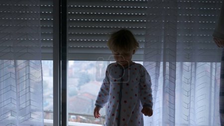 Photo for Baby toddler looking at automatic blinds going up, starting the day concept - Royalty Free Image