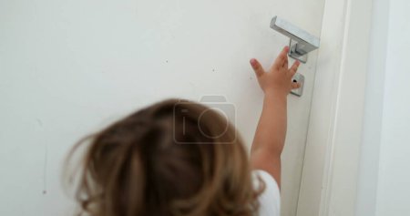 Foto de Bebé tratando de alcanzar la perilla de la puerta. Niño en puntas de los pies alcanzando la puerta - Imagen libre de derechos
