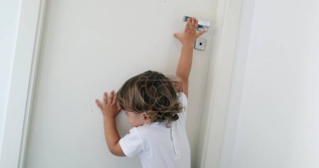 Foto de Bebé tratando de alcanzar la perilla de la puerta. Niño en puntas de los pies alcanzando la puerta - Imagen libre de derechos