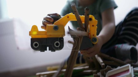 Téléchargez les photos : Kid joue avec bulldozer tracteur jouet cueillette des morceaux de bois jouer à la maison salle de jeux. Gros plan mains d'enfant - en image libre de droit