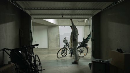 Person öffnet Garagentor und nimmt Fahrrad für eine Fahrt. Mutter schiebt Metalltor an Lagerraum und nimmt Fahrrad für Wochenendaktivitäten