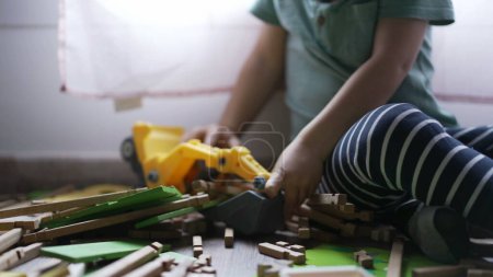 Téléchargez les photos : Kid joue avec bulldozer tracteur jouet cueillette des morceaux de bois jouer à la maison salle de jeux. Gros plan mains d'enfant - en image libre de droit