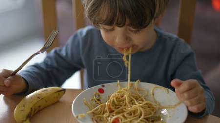 Photo for One small child eating pasta noodles by himself with fork. Kid eats lunch meal - Royalty Free Image