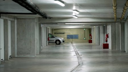 Foto de Coche saliendo de la plaza de aparcamiento del edificio subterráneo en vehículo gris blanco. Garaje interior moderno - Imagen libre de derechos