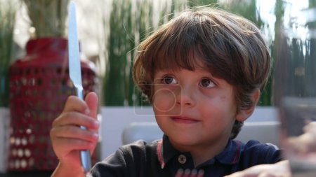 Téléchargez les photos : One little boy playing with knife at lunch table. Child misbehaving holding utensil. Dangerous concept - en image libre de droit