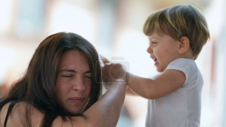 Photo for Mischievous child hurting mother. Parenting concept of mom being hit in the head by 2 year old toddler boy. Terrible two concept. Childhood stress concept - Royalty Free Image