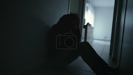 Photo for One anxious depressed woman covering face in despair sitting at home in the dark. Person suffering alone in corridor feeling shame and regret - Royalty Free Image