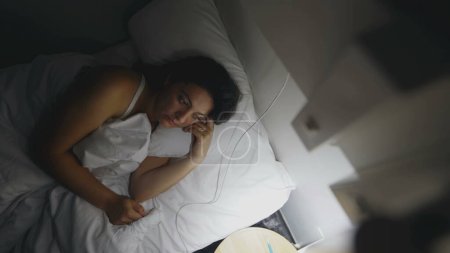 Pensive Woman laid in bed at night turns off lamp side. Thoughtful female person lying down going to sleep