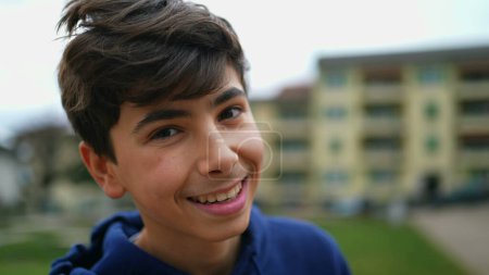 Téléchargez les photos : Portrait d'un adolescent heureux jeune garçon debout à l'extérieur au parc regardant la caméra dans le suivi des prises de vue. Gros plan d'un enfant mâle - en image libre de droit
