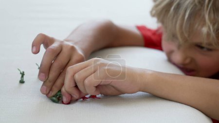 Téléchargez les photos : Gros plan de mains d'enfants jouant avec des figurines miniatures. Un petit enfant imaginatif joue avec des soldats jouets par lui-même - en image libre de droit