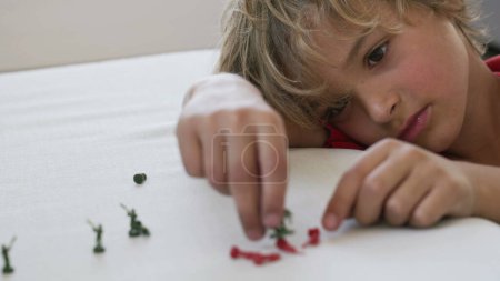 Téléchargez les photos : Petit garçon joue avec des figurines miniatures à la maison. Enfant jouant avec des soldats jouet près du visage - en image libre de droit