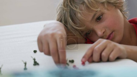 Téléchargez les photos : Petit garçon joue avec des figurines miniatures à la maison. Enfant jouant avec des soldats jouet près du visage - en image libre de droit