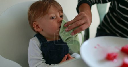 Téléchargez les photos : Infant one year old eating dessert, baby clapping hands. mother wiping toddler mouth with napkin - en image libre de droit