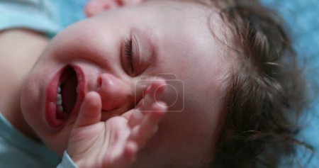 Photo for Tired baby rubbing eye and face with hands, sleepy child infant - Royalty Free Image