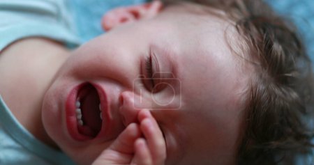 Upset tired crying baby. One year old infant child rubbing eye feeling exhausted