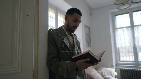Téléchargez les photos : Un homme lisant un livre appuyé sur un mur. Personne concentrée et étudiant à la maison - en image libre de droit