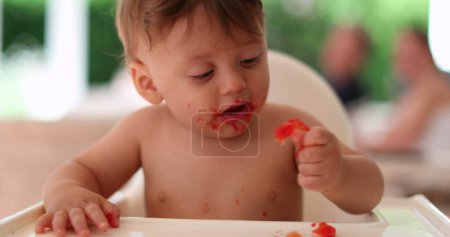 Téléchargez les photos : Cute messy baby eating by himself, shirtless toddler infant eating food - en image libre de droit