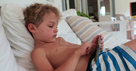 Téléchargez les photos : Jeune garçon couché sur le canapé à l'aide d'un smartphone - en image libre de droit