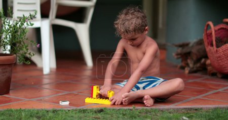 Photo for Creative child playing with building blocks outside in summer day. Toddler plays by himself - Royalty Free Image
