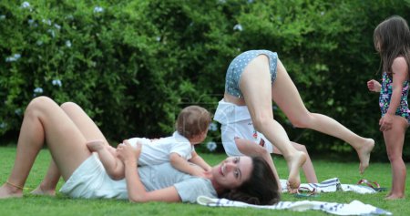 Téléchargez les photos : Mères dans la pelouse extérieure faisant de l'exercice de yoga avec les enfants et le bébé - en image libre de droit