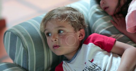 Photo for Children laid on sofa at night watching television screen - Royalty Free Image