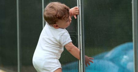 Photo for Cute baby blocked by pool security fence protection, drowning prevention - Royalty Free Image