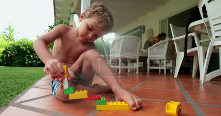 Téléchargez les photos : Enfant garçon jouant avec les blocs de construction ensemble à la maison, enfant franc joue avec par lui-même avec des pièces de construction - en image libre de droit