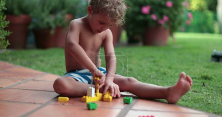 Photo for Child playing with building blocks outside in home garden - Royalty Free Image