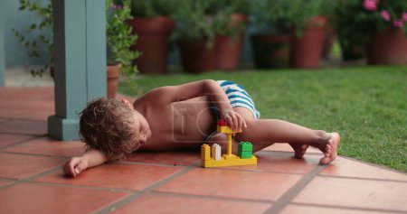 Photo for Child playing with building pieces in home balcony. Kid lying on floor - Royalty Free Image