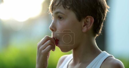 Foto de Guapo joven comiendo fruta y masticando mientras mira a la cámara sonriendo con la boca llena - Imagen libre de derechos