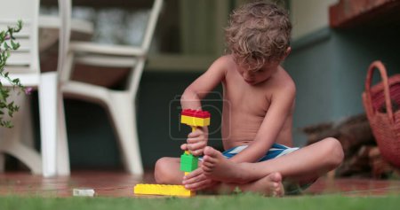 Téléchargez les photos : Enfant imaginatif jouant avec les blocs de construction à l'extérieur. Tout-petit garçon joue avec des morceaux de construction - en image libre de droit