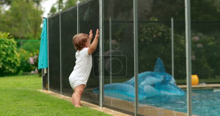 Photo for Baby wanting to go inside swimming pool water, blocked by security fence protection, drowning prevention - Royalty Free Image