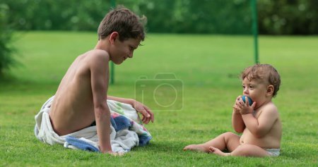 Téléchargez les photos : Frères et sœurs ensemble dans la cour d'herbe extérieure, enfant avec petit frère - en image libre de droit