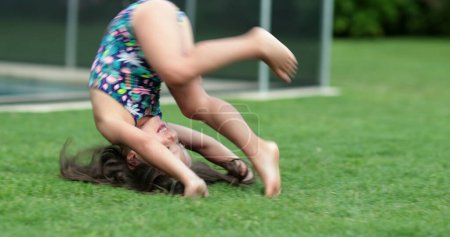 Téléchargez les photos : Enfant fille faisant un saut périlleux à l'extérieur. Petit enfant qui tombe dehors dans l'herbe - en image libre de droit