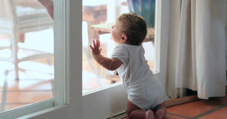 Photo for Infant baby leaning on home window, toddler wanting to go outside - Royalty Free Image
