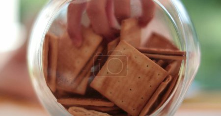 Foto de Primer plano de las manos del niño tomando galletas saladas del frasco de vidrio interior - Imagen libre de derechos