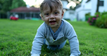 Téléchargez les photos : Bébé se retournant et rampant vers la caméra. Enfant en bas âge dans le jardin extérieur de la maison - en image libre de droit