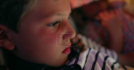 Téléchargez les photos : Gros plan sur le visage de l'enfant devant l'écran de l'appareil la nuit avant de se coucher - en image libre de droit