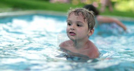 Foto de Familia en la piscina en un caluroso día de verano. Niño pequeño dentro del agua con toalla - Imagen libre de derechos