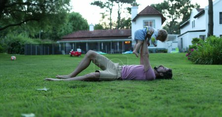 Téléchargez les photos : Père tenant et soulevant bébé tout-petit bébé dans l'air, maison résidentielle en arrière-plan - en image libre de droit