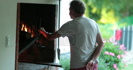 Photo for Senior retired man preparing BBQ grill. Older person in front of fire cooking parilla - Royalty Free Image