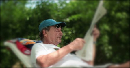 Téléchargez les photos : Un homme plus âgé lisant un journal dehors dans la nature. Retraité senior lisant nouveau. - en image libre de droit