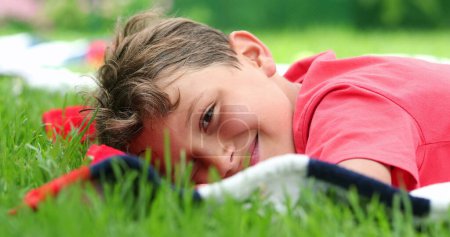 Photo for Young handsome child boy lying down on grass outdoors, kid resting and relaxing - Royalty Free Image
