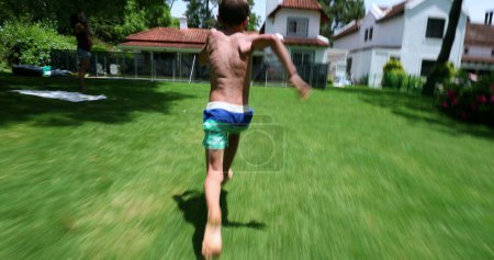 Téléchargez les photos : Enfant courir à l'extérieur dans la pelouse de la maison et sauter dans l'eau de la piscine - en image libre de droit