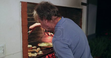Téléchargez les photos : Retired older man managing grill BBQ parilla at night. Senior man preparing food - en image libre de droit