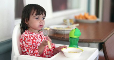Foto de Niña pequeña comiendo fruta de melón en la trona - Imagen libre de derechos